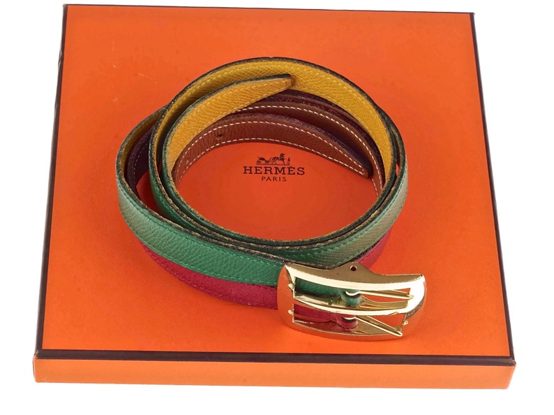 Pode incluir: Um cinto de couro multicolorido com uma fivela dourada. O cinto est&aacute; dobrado e apresentado numa caixa laranja com o logotipo da Hermes Paris.