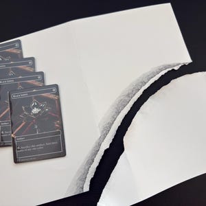 May include: Four Black Lotus trading cards are arranged on a white surface, with a torn white paper in the background. The cards feature a black background with a white lotus flower and gold accents. The text "Black Lotus" is visible.