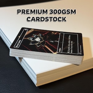 May include: A stack of Black Lotus trading cards with a black background and gold accents. The cards are on top of a stack of white cardstock. The text "PREMIUM 300GSM CARDSTOCK" is displayed above the cards.