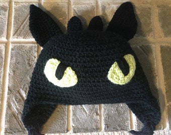 May include: Black crocheted hat with green eyes, resembling a dragon.