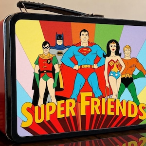 May include: A rectangular metal lunchbox with a black frame and handle, featuring a colourful graphic of Robin, Batman, Superman, Wonder Woman, and Aquaman. The text SUPER FRIENDS is printed in large yellow letters across the bottom of the front panel.