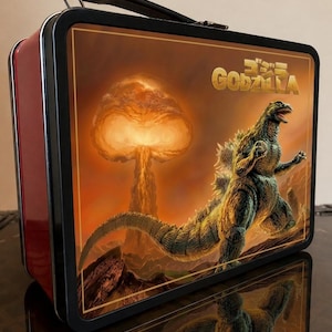May include: A rectangular metal lunch box with a black frame and handle. The front panel features a graphic of Godzilla standing in a rocky landscape with a large orange mushroom cloud in the background and the text Godzilla in gold lettering.