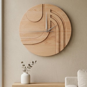 May include: A large, round wooden wall clock with a geometric design. The clock features a light brown finish and silver-colored hands. The design includes layered, curved shapes. The clock is mounted on a beige wall.