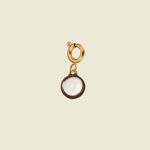 Op de afbeelding: Een goudkleurige veerringsluiting bevestigd aan een kleine, ronde bedel met een wit, glad, rond middenelement dat is omvat door een donkerbruine rand. De bedel hangt verticaal aan de ronde sluiting en vormt een eenvoudig sieraadonderdeel.