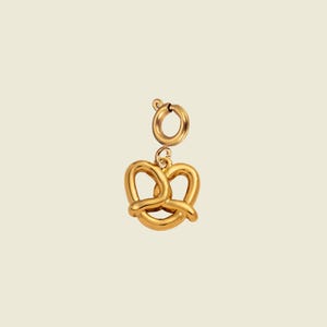 May include: A gold-toned metal charm shaped like a twisted pretzel, featuring a smooth, polished surface. The charm is attached to a circular spring ring clasp, allowing it to be easily connected to a bracelet, necklace, or other jewelry item.