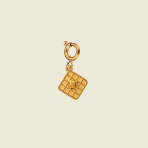 Puede incluir: Un dije de tono dorado con forma de gofre cuadrado con un pequeño trozo de mantequilla cuadrado en el centro. El dije está unido a un cierre de anilla circular y presenta una textura de rejilla en la superficie del colgante con forma de gofre.
