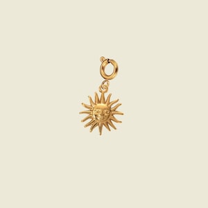 Peut inclure: Un charm doré représentant un soleil souriant avec des rayons. Le charm a un visage détaillé et est attaché à un petit fermoir rond. Le charm est probablement destiné à un collier ou un bracelet.