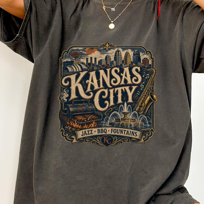 K&ouml;nnte beinhalten: Dunkelgraues T-Shirt mit einem Vintage-Grafikdesign von Kansas City. Das Design zeigt die Skyline der Stadt, einen Grill, ein Saxophon und einen Brunnen, mit den Worten "Kansas City" und "Jazz BBQ Fountains".