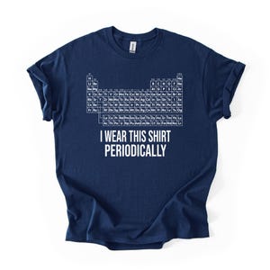 May include: A navy blue short-sleeved t-shirt featuring a white graphic of the periodic table of elements printed on the chest. Below the table, the text reads I WEAR THIS SHIRT PERIODICALLY in a bold, white, sans-serif capital letter font.