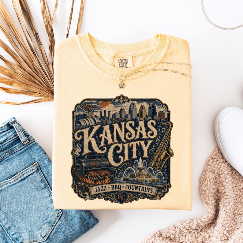 K&ouml;nnte beinhalten: Ein hellgelbes Comfort Colors T-Shirt mit einem Grafikdesign im Vintage-Stil von Kansas City. Das Design zeigt die Skyline der Stadt, ein Saxophon, einen Grill und die Worte "Kansas City, Jazz, BBQ, Fountains."