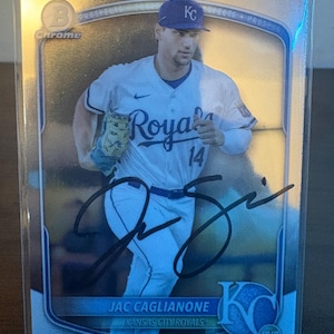 Può includere: Una figurina da baseball Bowman Chrome raffigurante Jac Caglianone dei Kansas City Royals. La carta mostra un giocatore in divisa bianca con il numero 14, un berretto blu e un autografo a inchiostro nero sul davanti. La carta include il testo.