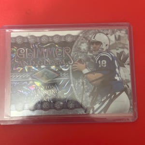 May include: A white ceramic mug with a black handle and the text "But First, Coffee" in a bold, black font. The mug is set against a blurred background, suggesting a cozy setting.