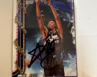 Può includere: Una carta collezionabile di basket Topps con Ace Bailey degli Utah Jazz. La carta ha un design festivo natalizio con fiocchi di neve e un bordo a ghirlanda. Il giocatore è mostrato con le braccia alzate e la carta è autografata.