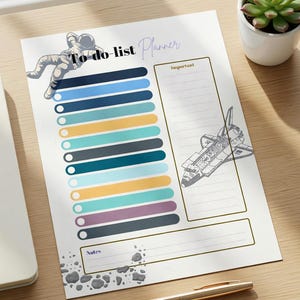 May include: A to-do list planner with an astronaut illustration and the words "To-do list Planner". The planner has a section for important notes and a space shuttle graphic. A gold pen rests on the wooden surface.