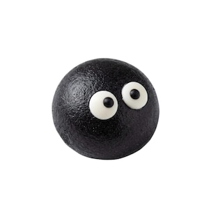 Op de afbeelding: Een bolvormig object met een getextureerd zwart oppervlak, voorzien van twee witte ronde ogen met kleine zwarte pupillen aan de rechterkant. Het item heeft een gladde, ronde vorm en een matte afwerking, lijkend op een klein, donker wezen.