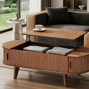 May include: A wooden lift-top coffee table with a light brown finish. The table has a storage compartment with two folded blankets inside. The table is in front of a sofa and a small side table.