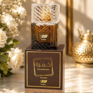 May include: A rectangular glass perfume bottle with a textured pattern and a clear cap, resting on a brown cardboard box. The box features gold text reading Khamrah Qahwa, Momin, and Eau de Parfum, with a volume of 30 ml and 1.01 fl. oz printed.