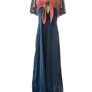 Op de afbeelding: Een maxi-jurk in vintage-stijl, in tealblauw, met een roze lijfje en grijze kapmouwen. De jurk wordt op een mannequin getoond en toont zijn vloeiende silhouet en retro-ontwerp.