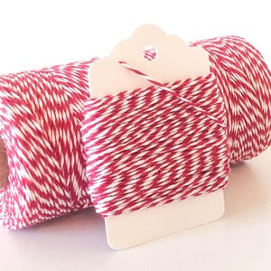 May include: A large spool of red and white twisted twine alongside a smaller, flat white cardboard card wrapped with the same red and white twine. The twine features a consistent, alternating pattern of red and white fibers twisted together.
