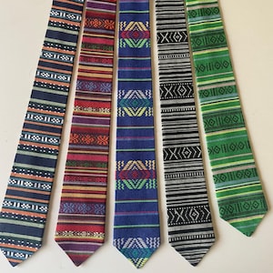 May include: Five patterned neckties in a row. The ties feature various designs, including stripes and geometric patterns, in colors like navy, red, blue, black, and green. The ties are made of a woven fabric.