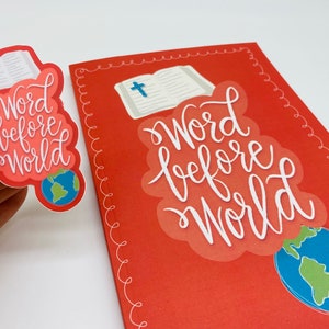 May include: A red card with a white border and the words "Word before world" in white script. A white open book with a blue cross is behind the words. A blue and green globe is below the words. A sticker with the same design is shown in the upper left corner.