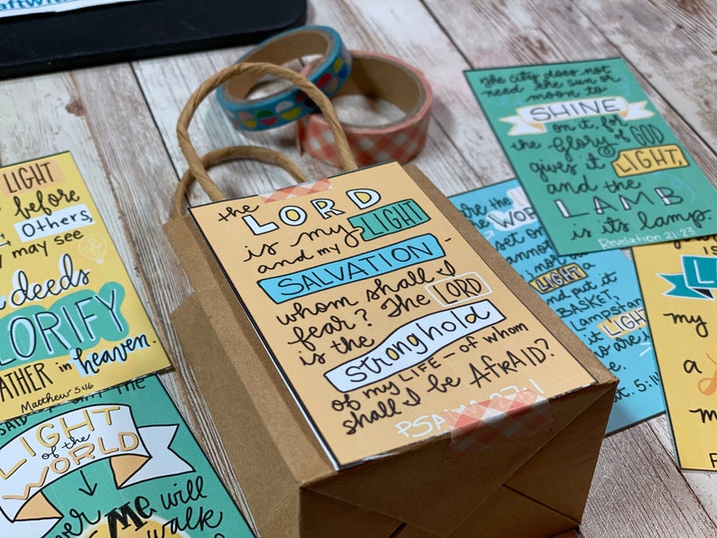 May include: A brown paper gift bag with a yellow and blue card attached. The card has the text "The Lord is my light and my salvation - whom shall I fear? The Lord is the stronghold of my life - of whom shall I be afraid?"  The bag is decorated with a pink and white gingham ribbon.