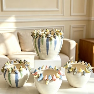 May include: Three ceramic planters with a cream-colored base and vertical brushstrokes in blue and green. Each planter features a decorative rim adorned with small, sculpted ceramic snails and birds in various pastel colors around the top edge.
