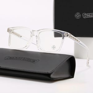 May include: Clear rectangular eyeglasses with silver accents and a decorative emblem on the frame. The glasses rest on a black leather case. A black box with a logo is in the background.