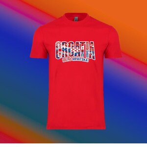 May include: A red t-shirt with the word "CROATIA" in a multi-colored design, with the Croatian flag incorporated into the letters. Below the word is the text "IDEMO HRVATSKA!"