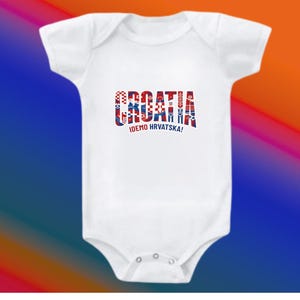 May include: White baby bodysuit with the word "CROATIA" in red, white, and blue, with the text "IDEMO HRVATSKA!" below. The bodysuit has short sleeves and a snap closure. The background is a gradient of blue, red, and orange.
