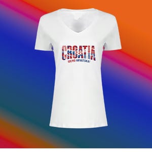 May include: White V-neck t-shirt with the word "CROATIA" in red, white, and blue, and the text "IDEMO HRVATSKA!" below. The shirt has short sleeves and a simple design.