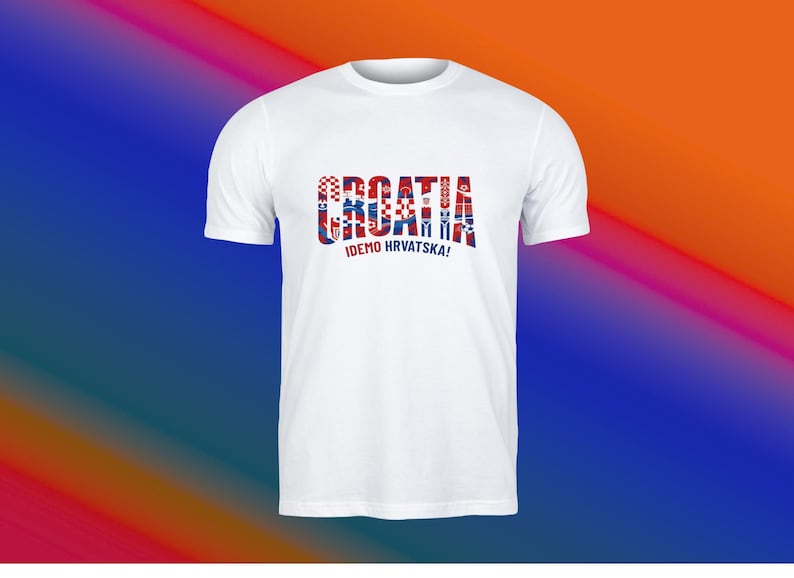 May include: White t-shirt featuring the word "CROATIA" in red, white, and blue, with a Croatian flag design. Below the word is the phrase "IDEMO HRVATSKA!" in black. The shirt has short sleeves.