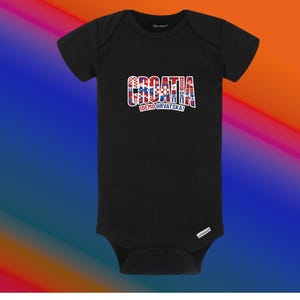 May include: Black baby bodysuit with the word "CROATIA" in red, white, and blue, with the Croatian flag colors. Below the word "CROATIA" is the text "IDEMO HRVATSKA!" in white. The bodysuit is made of soft material.