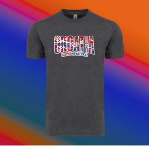 May include: Dark gray t-shirt with the word "CROATIA" in a red, white, and blue design, with the text "IDEMO HRVATSKA!" below. The shirt has a crew neck and short sleeves.