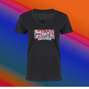May include: Black V-neck t-shirt with the word "CROATIA" in a red, white, and blue design. The text "IDEMO HRVATSKA!" is below the word "CROATIA". The shirt has short sleeves.