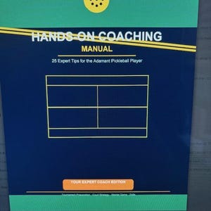 Può includere: Un manuale intitolato "HANDS-ON COACHING" con il sottotitolo "25 consigli esperti per il giocatore di pickleball Adamant". La copertina è blu scuro con una grafica gialla del campo da pickleball e testo. Sono visibili anche le parole "YOUR EXPERT COACH EDITION".
