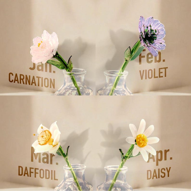 May include: Four glass flowers in small clear vases, each labeled with a month and name: Jan. Carnation, Feb. Violet, Mar. Daffodil, and Apr. Daisy. The flowers are crafted with delicate petals in pink, purple, white, and yellow, featuring green stems.