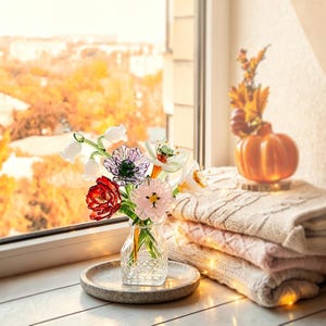 May include: A clear glass vase with a diamond-patterned base holds a bouquet of colorful glass flowers, including white lily of the valley, a purple anemone, a red tulip, a pink blossom, and a white daffodil, all with green glass stems.