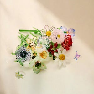 May include: A collection of handcrafted glass flowers featuring various species including daisies, lilies, and poppies with green stems. The arrangement includes a small glass butterfly and a delicate white floral ring, all rendered in vibrant, translucent colors.