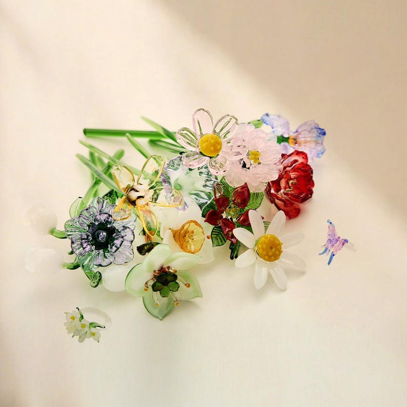 May include: A collection of handcrafted glass flowers featuring various species including daisies, lilies, and poppies with green stems. The arrangement includes a small glass butterfly and a delicate white floral ring, all rendered in vibrant, translucent colors.