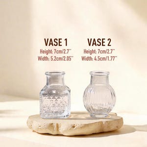 May include: Two clear glass vases. Vase 1 has a square base with a diamond pattern, height 2.7 inches, width 2.05 inches. Vase 2 has a round, ribbed body, height 2.7 inches, width 1.77 inches. Text labels VASE 1 and VASE 2 are displayed above.