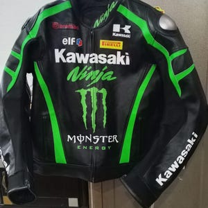 Könnte beinhalten: Schwarze Motorradjacke aus Leder mit grünen Akzenten und Kawasaki Ninja-Branding. Mit Logos von Sponsoren wie Brembo, Elf und Pirelli. Die Jacke hat ein Monster Energy-Logo und Kawasaki-Branding auf den Ärmeln.