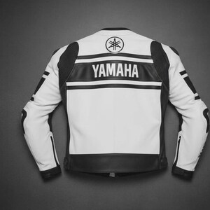Puede incluir: Una chaqueta de moto blanca y negra con el logotipo y el texto de Yamaha en la parte posterior. La chaqueta tiene mangas largas con detalles negros en los hombros y brazos, cuello alto y una franja negra horizontal en la parte superior de la espalda.