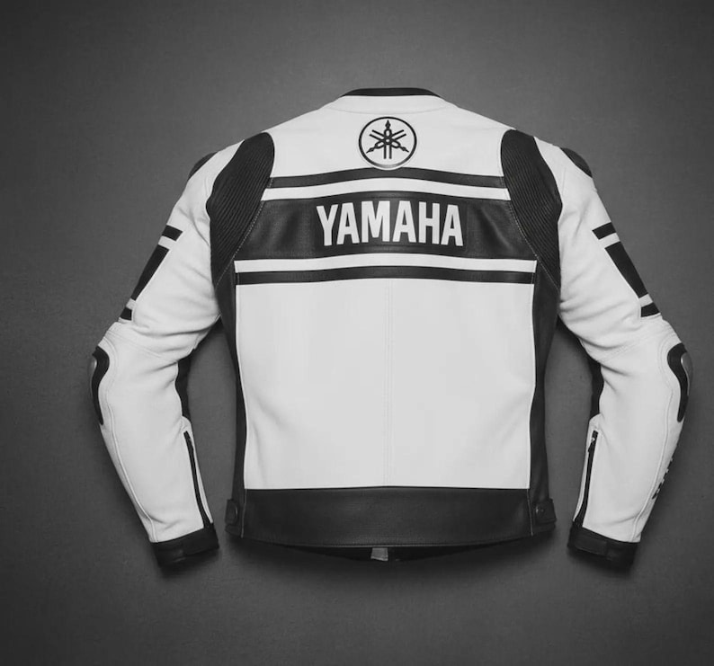 Puede incluir: Una chaqueta de moto blanca y negra con el logotipo y el texto de Yamaha en la parte posterior. La chaqueta tiene mangas largas con detalles negros en los hombros y brazos, cuello alto y una franja negra horizontal en la parte superior de la espalda.