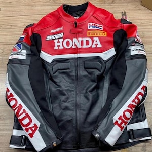 May include: A black, red, and gray Honda motorcycle racing jacket. The jacket features the Honda logo in white across the chest, with additional logos for Showa, HRC, and Pirelli. The sleeves have the Honda logo in red.
