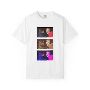 Puede incluir: Camiseta blanca con un diseño gráfico de tres imágenes apiladas verticalmente. Cada imagen muestra a una pareja mirándose. La imagen superior tiene una sudadera con capucha roja, la imagen central una sudadera con capucha marrón y la inferior una sudadera con capucha rosa.