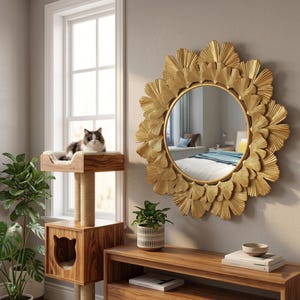 Peut inclure: Un miroir mural rond doré avec un motif décoratif de feuilles. Un arbre à chat en bois avec un panier et des poteaux à gratter est à côté d'une fenêtre. Un chat se repose sur l'arbre à chat. Une console en bois avec une plante en pot est en dessous du miroir.