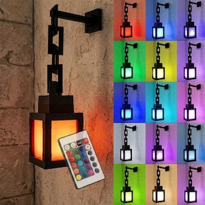 May include: Black wall-mounted lantern with a rectangular design, emitting a warm orange glow. A remote control with multiple color options is visible. Additional lanterns in various colors are displayed in the background, showcasing the lantern's color-changing capabilities.
