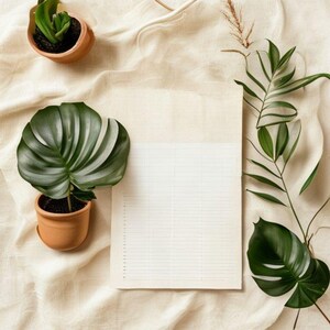 May include: An overhead shot of a neutral-toned composition featuring a lined paper, potted plants, and greenery. The plants include a large, dark green Monstera leaf and smaller succulents in terracotta pots. The background is a beige fabric.