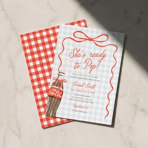 Puede incluir: Invitación para baby shower con un patrón de cuadros rojos y blancos en la parte posterior. La parte delantera presenta un fondo de cuadros azul claro con texto rojo y una ilustración de botella de cola. El texto dice "She's ready to Pop!" y detalles del evento.